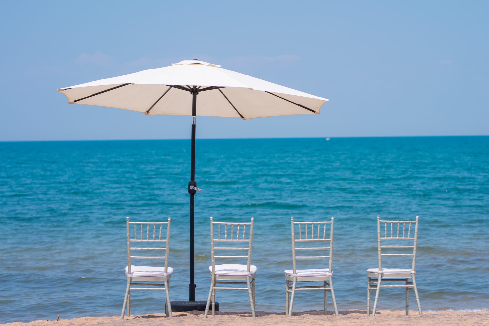 White chairs and a beach umbrella set up on the golden sands overlooking Lake Malawi’s clear blue waters.
