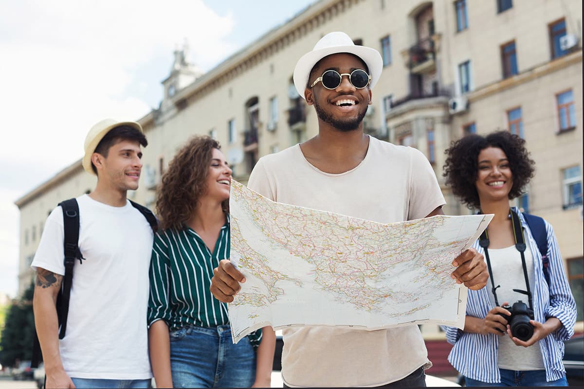 Happy group of tourists with map and camera exploring city streets on vacation.