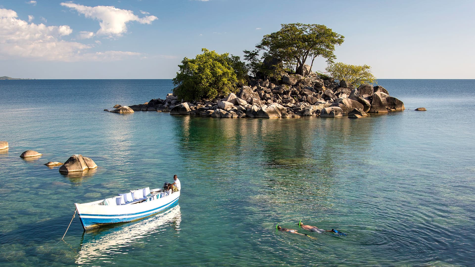 Tourists snorkeling near a rocky island in Lake Malawi with a boat anchored nearby